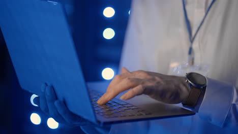 Male-network-engineer-doing-a-system-check-standing-in-the-server-room-with-his-laptop.-At-data-center-men-server-specialists-inspecting-working-system-and-hardware-of-rack-server-computer-cabinets