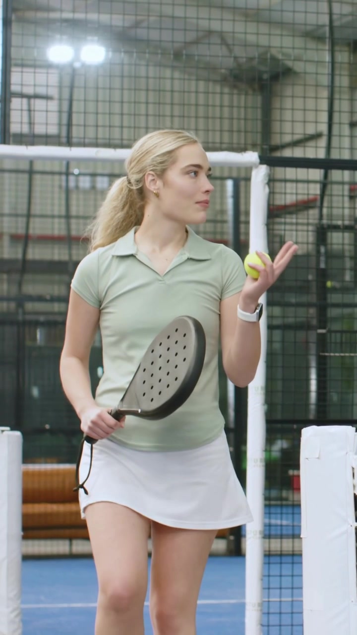 Vertikal video: Partner veileder, kvinne i pikétrøye flytter nett på bane, forbereder serve med racket og ball.