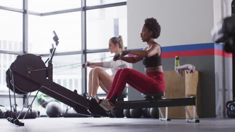 Video-of-two-diverse,-confident-women-on-rowing-machines-working-out-at-a-gym