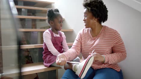 happy african american mother advising and tying shoes of daughter at home, slow motion