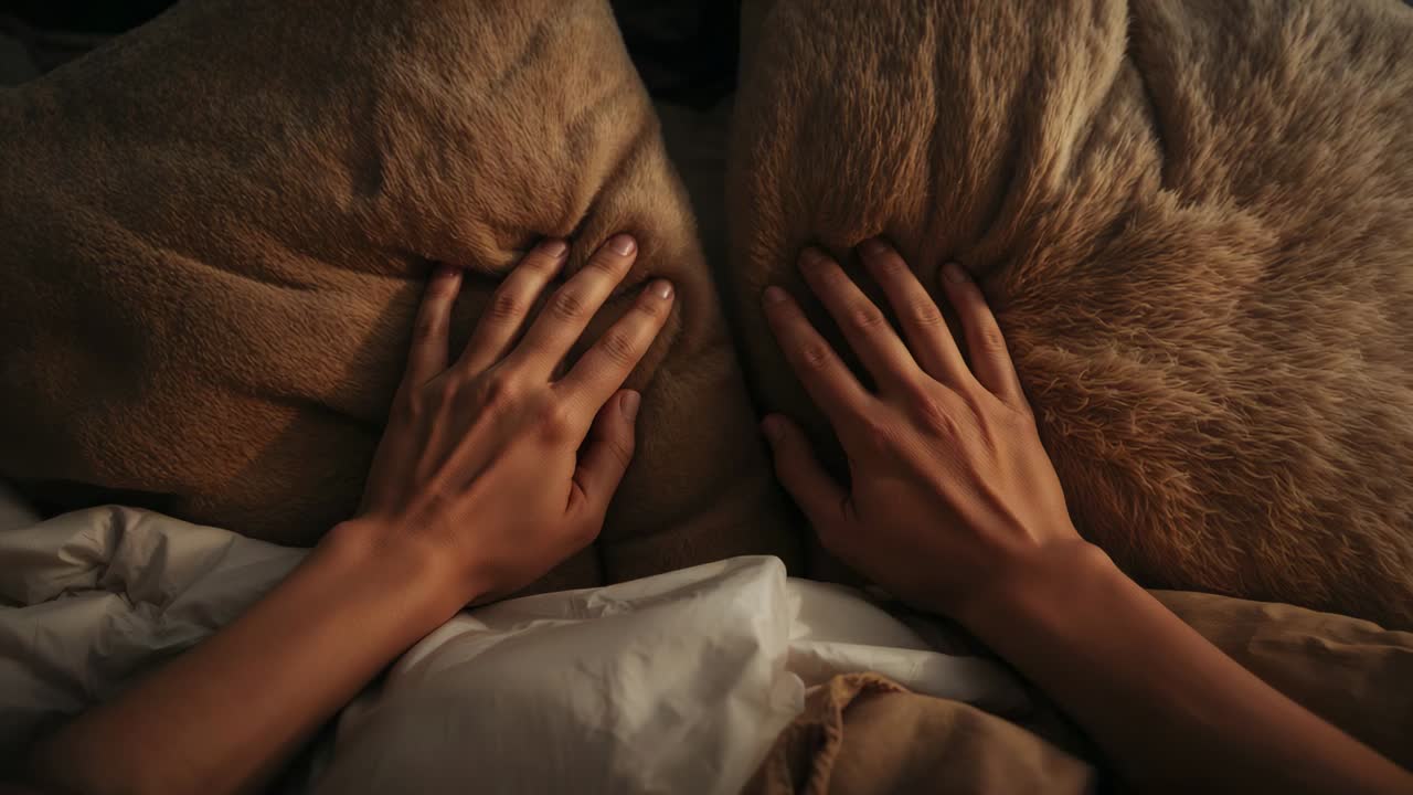 Manos delgadas de adulto colocando y comprimiendo dos almohadas grandes peludas en la cama, manteniéndolas en su sitio