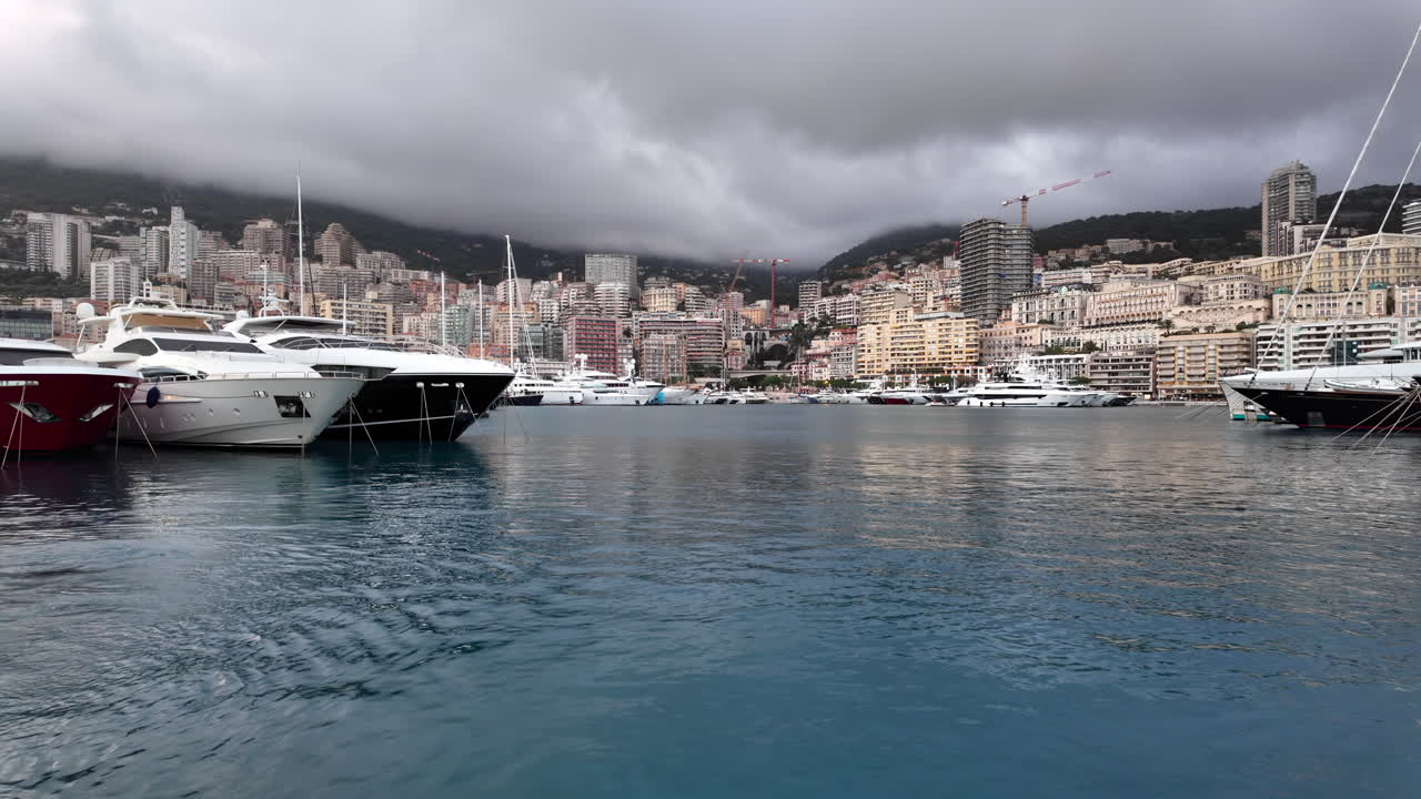 La Condamine, Monaco - July 4, 2025: Row of sleek luxury yachts, docked in Port Hercules with the Monaco cityscape and misty hills in the background