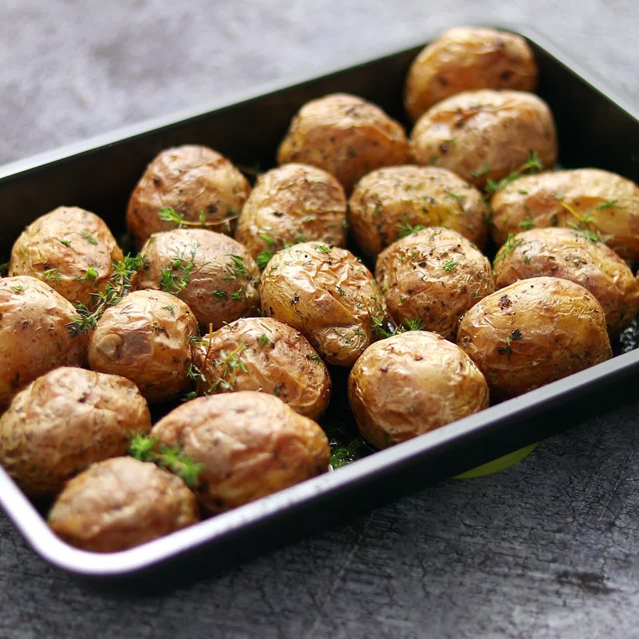 Patate intere al forno fatte in casa con la buccia, con burro, rosmarino e timo. Servite in un piatto di metallo.