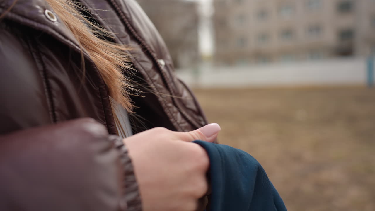 쌀쌀한 동네에서 비니를 쓴 여성이 따뜻한 겨울 액세서리를 착용한 손을 클로즈업한 모습, 겨울 동안 조용한 교외 풍경 속에서 니트 모자를 섬세하게 만지고 있어요.