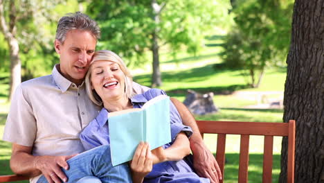 Affectionate-couple-sitting-on-park-bench-reading