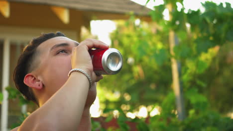 closeup portrait of attractive young hispanic young adult drinking can of soda, green trees background