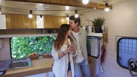 Happy-couple-enjoying-time-together-in-small-kitchen-in-van.-Family-husband-and-wife-drinking,-celebrating-romantic-anniversary-together,-kissing-at-wheels-house-vacation