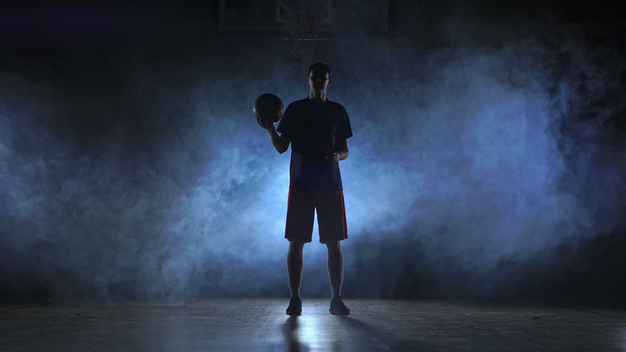 imágenes cercanas de un jugador de baloncesto girando la pelota en su dedo, habitación oscura y brumosa con reflector