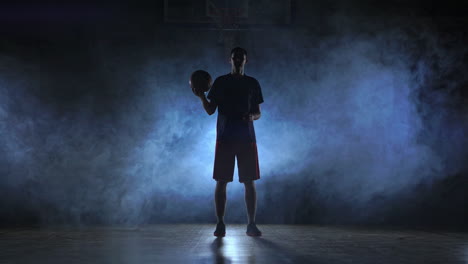 Close-footage-of-basketball-player-spinning-ball-on-his-finger,-dark-misty-room-with-floodlight