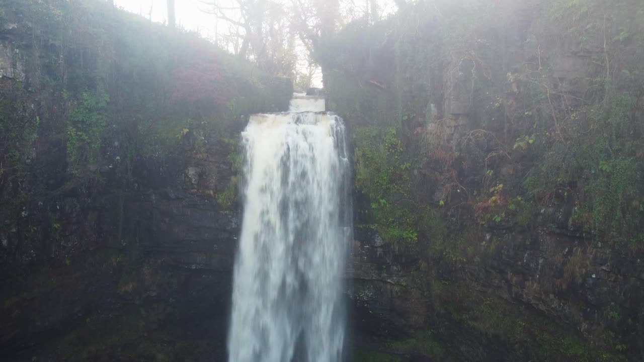 영국 웨일즈 4k의 빠른 강과 황금빛 태양을 드러내기 위해 공중 드론이 천천히 상승하는 일출의 폭포