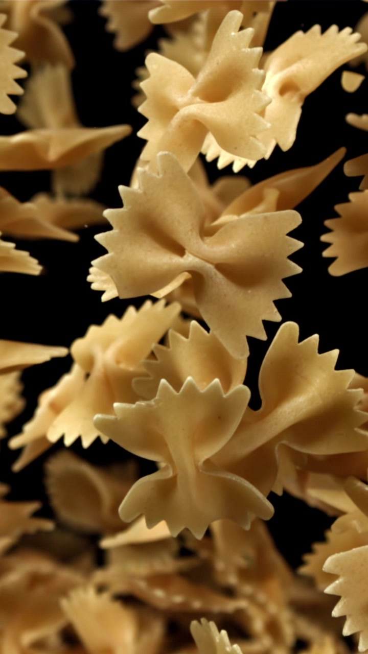 Pasta farfalle cruda che cade al rallentatore su uno sfondo nero