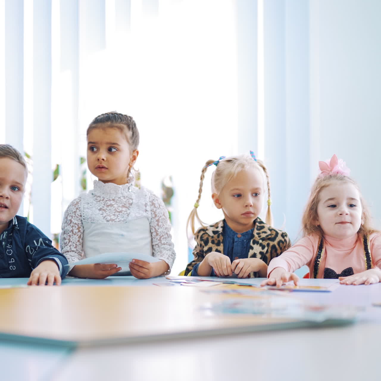 Group of little students at a circle table during the lesson. Children learning English together in games at primary school.