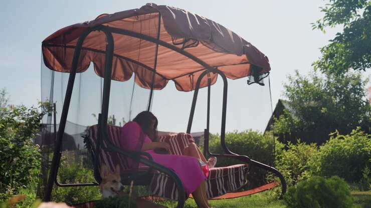 Donna che legge in un giardino tranquillo, ambiente silenzioso con donna che legge piacevolmente sotto un baldacchino, scena serena di donna sdraiata su un'altalena circondata da fiori e dalla luce del sole