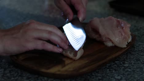 Cutting-and-butterflying-a-piece-of-chicken-breast-on-a-wooden-cutting-board