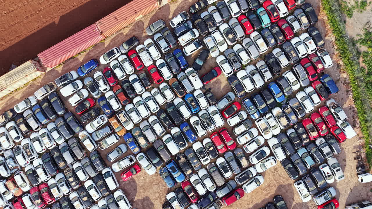 Bilparkeringsplads med mange parkerede køretøjer i forskellige farver og størrelser om dagen på et åbent område
