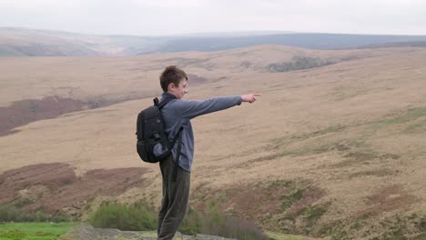 Young-boy-outdoors-standing-on-a-countryside-hill-top,-admiring-the-moorland-views