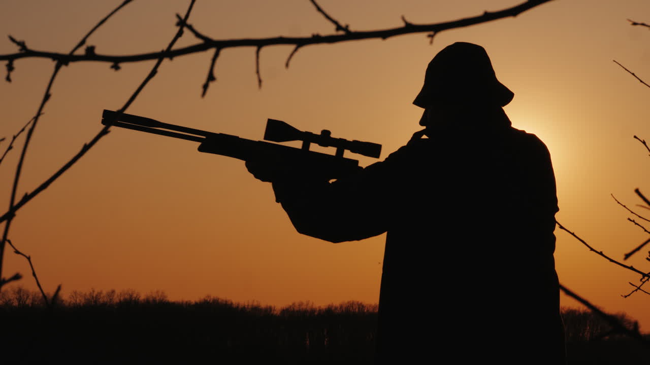 총을 든 사냥꾼의 실루엣 태양 광선이 그의 얼굴에 빛난다