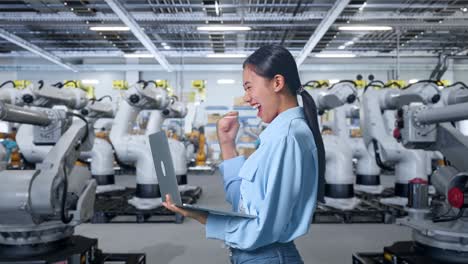 ingeniero feliz usando una computadora portátil en una fábrica con robots