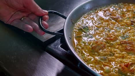 el chef mueve el arroz de la paella cocinando en una paellera.