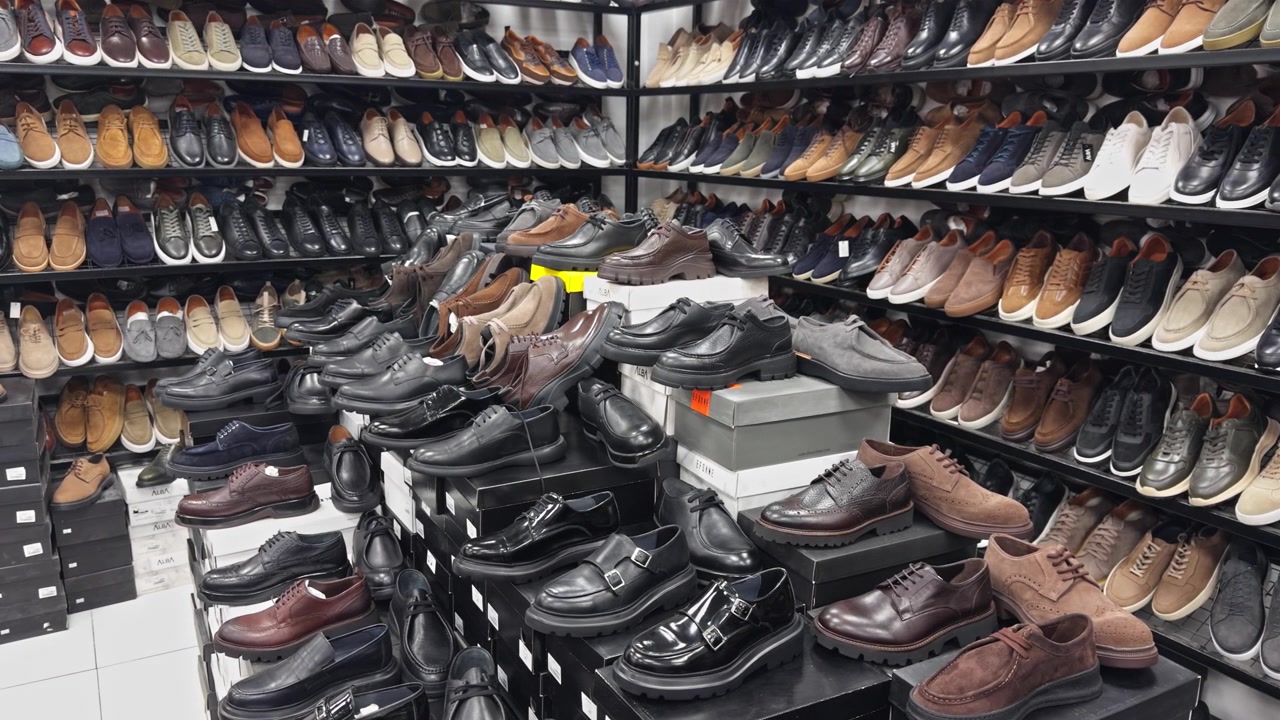 Hochwertige 4K-Weitwinkelaufnahme eines Schuhgeschäfts, gefüllt mit verschiedenen eleganten Herren-Lederschuhen, Stiefeln und Turnschuhen. Perfekt für Mode-, Einzelhandels- und Einkaufskonzepte
