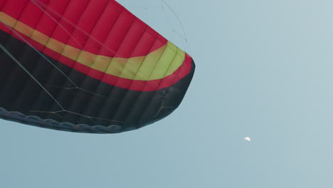 colorful paraglider canopy graceful drifting across vast twilight sky with half moon overhead soft dusk light contrasting delicate rigging against serene cloud backdrop