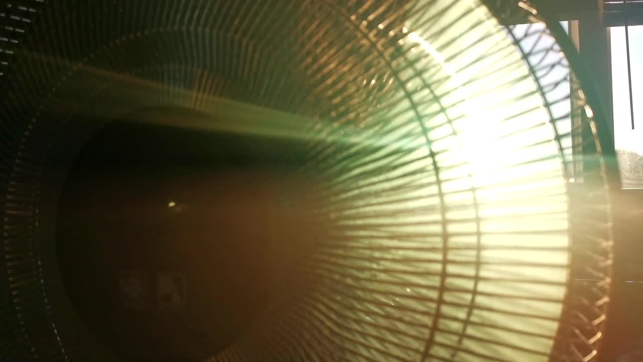 Dusty indoor fan during sunset. Low sun breaking through grid and propellers of ventilator causing lens flares.