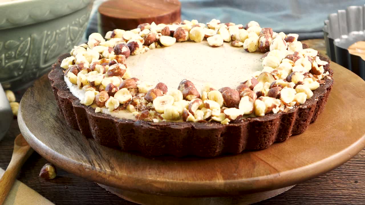 A delicious dessert, Coffee Hazelnut Cream Tart. Made with espresso powder, chocolate crust and loaded with crushed hazelnut. Close up of sliding the pie or cake across the wooden counter top