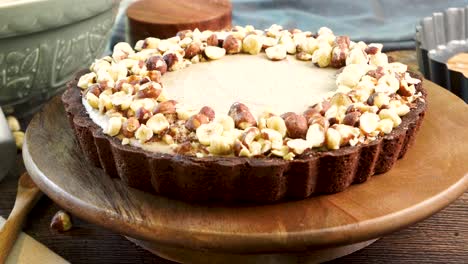 a delicious dessert, coffee hazelnut cream tart. made with espresso powder, chocolate crust and loaded with crushed hazelnut. close up of sliding the pie or cake across the wooden counter top