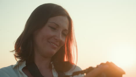 close up of young woman taking photograph during golden hour with intense focus, gentle backlight outlining hair and camera details, serene outdoor setting filled with warm ambient glow