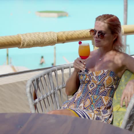 cheerful woman with cocktail resting on hotel balcony