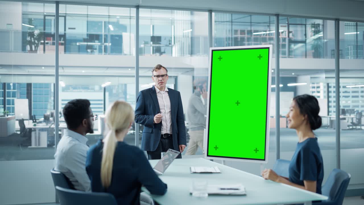 el gerente de operaciones de la compañía realiza una presentación de la reunión para un equipo de economistas. hombre adulto utiliza pizarra digital con pantalla verde vertical para mostrar la maqueta. la gente trabaja en una oficina de negocios.