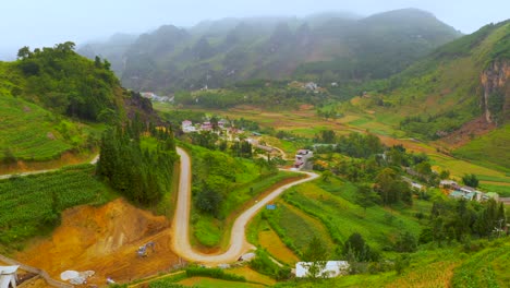 Aerial-dolly-forward-of-a-winding-road-cut-into-the-mountainside-of-the-misty-mountains-on-the-Dong-Van-Karst-plateau-geopark