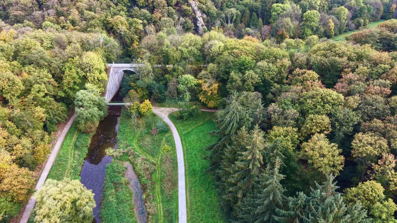 Luftaufnahme eines dichten Waldes, der von einer schmalen Straße in der Nähe der Landschaft von Saint Berthevin durchquert wird, wobei nach links geschwenkt wird, um eine Brücke zu zeigen