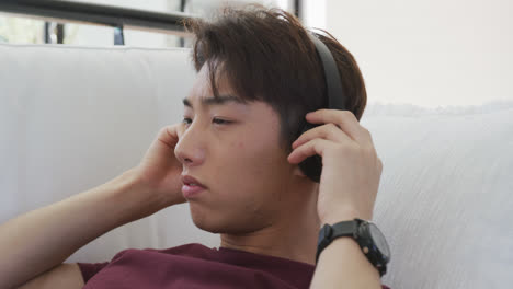 아시아 남성 십대가 거실에서 헤드폰으로 음악을 듣고 있습니다.