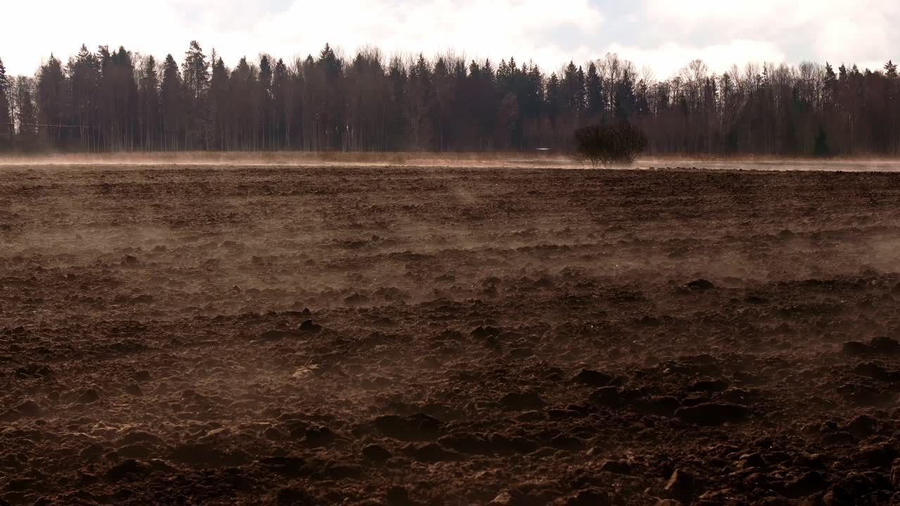 Early spring drone shot over ploughed field with low fog drifting across rich soil