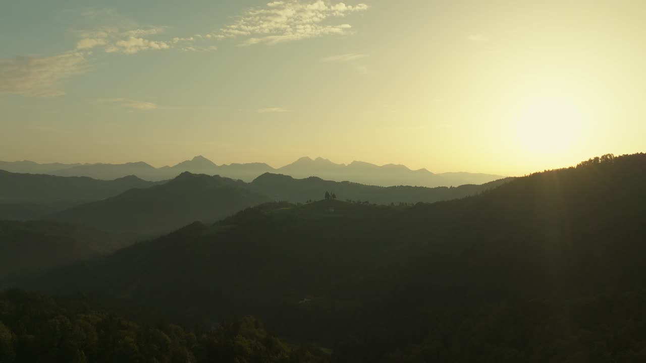 Sunrise over St Thomas Church in the Slovenian Alps with distant mountain peaks in view