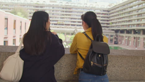 Rear-View-Of-Two-Young-Female-Friends-Visiting-The-Barbican-Centre-In-City-Of-London-Taking-Photo-On-Mobile-Phone-4