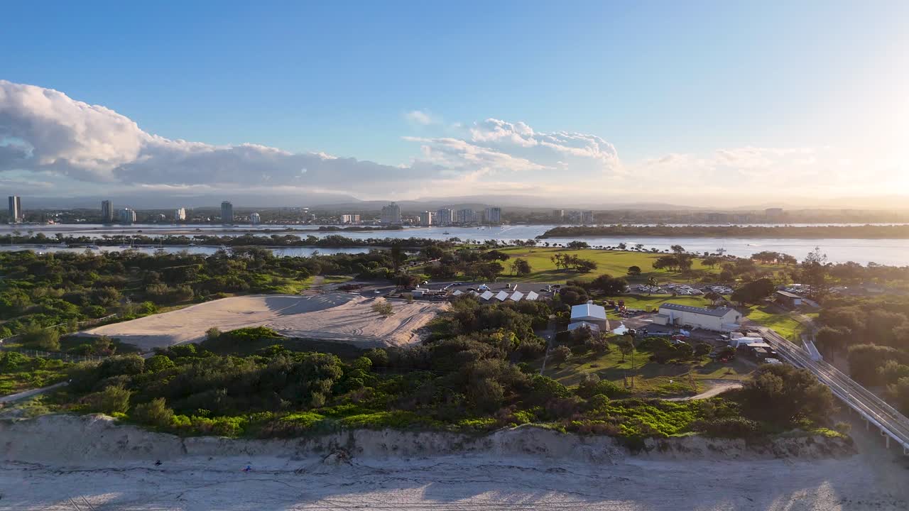 Drone footage captures Gold Coast's beach, greenery, and skyline under clear skies with soft lighting, showcasing natural beauty and urban landscape