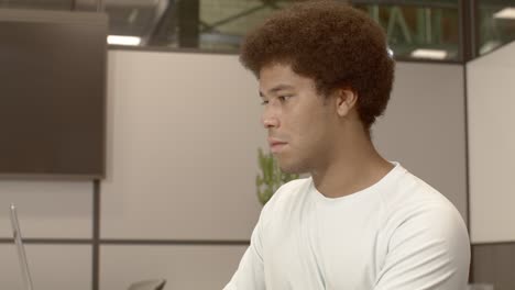 african american male in is 20's typing on a computer in an office with video dolly back