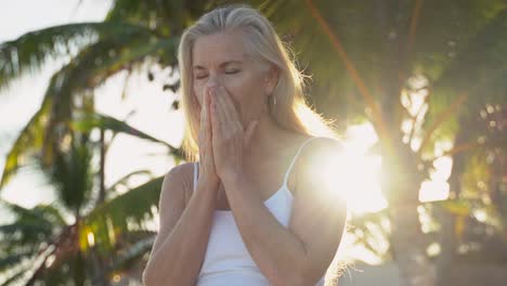 el sol brilla en la lente de la cámara mientras una mujer rubia madura se ve asombrada fuera de la cámara, luego sonríe a la cámara y luego vuelve a mirar fuera de la cámara con una palmera detrás