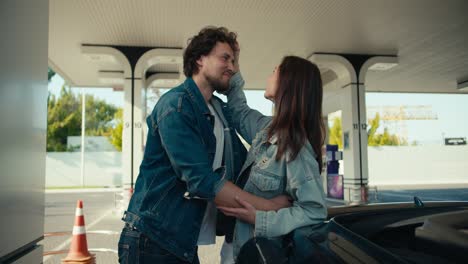 romantic communication while refueling their car: a guy and a girl chat and flirt at a gas station near their dark gray