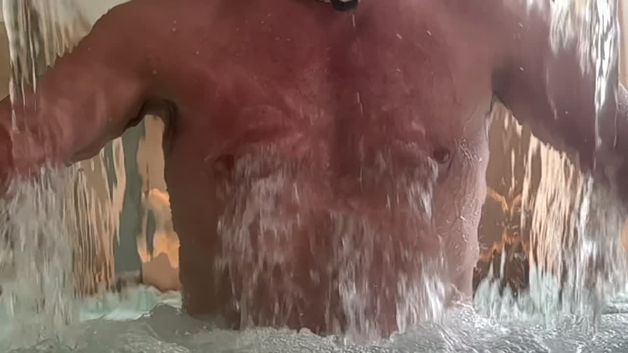 A slow motion closeup view of the chest of an adult man through a waterfall at a Spa.