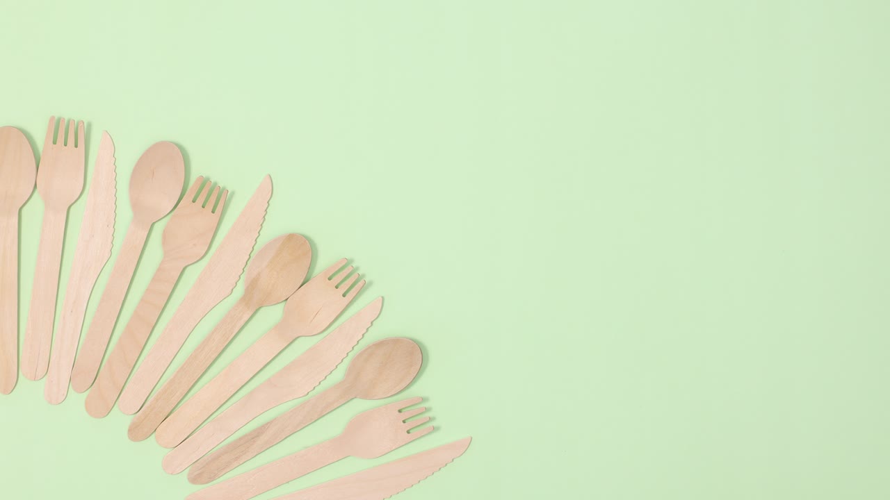 una pila de utensilios de cocina ecológicos y sin residuos bailan y se mueven sobre un fondo verde claro.