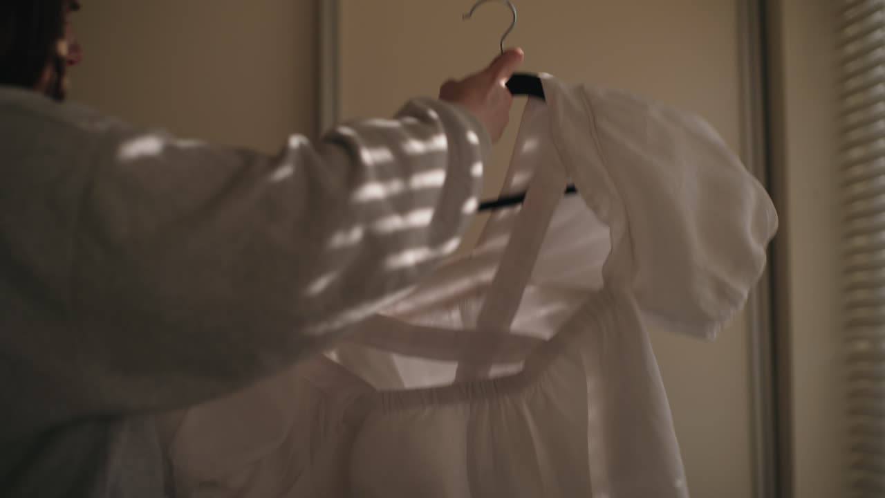Woman hangs a clean shirt on a hanger in soft, moody Irish light. A quiet, domestic moment with warm natural tones and shadow texture.
