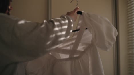 woman hangs a clean shirt on a hanger in soft, moody irish light. a quiet, domestic moment with warm natural tones and shadow texture.