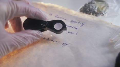 a forensic detective's hand holding a magnifying glass examines a handwritten letter from the zodiac