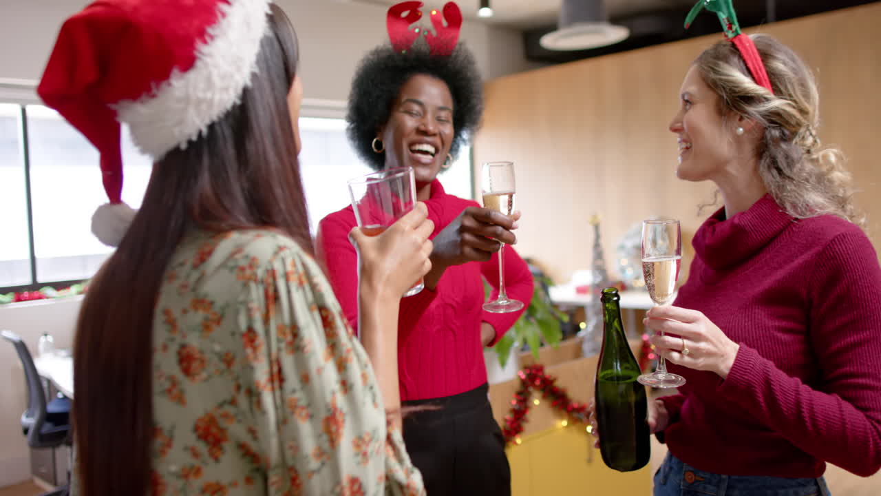 Happy diverse female creative colleagues drinking christmas toast in office, slow motion