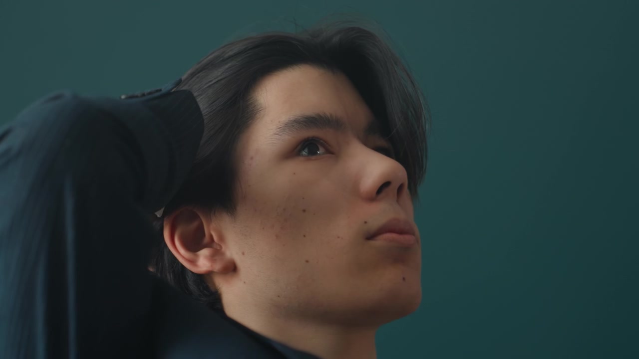 Uomo asiatico che si sistema i capelli in abito, sequenza di ritratti introspettivi con uno sfondo teal suggestivo, ombra drammatica e luce di contorno soffusa, gesti contemplativi e mani posate, provino d'attore e creativo.