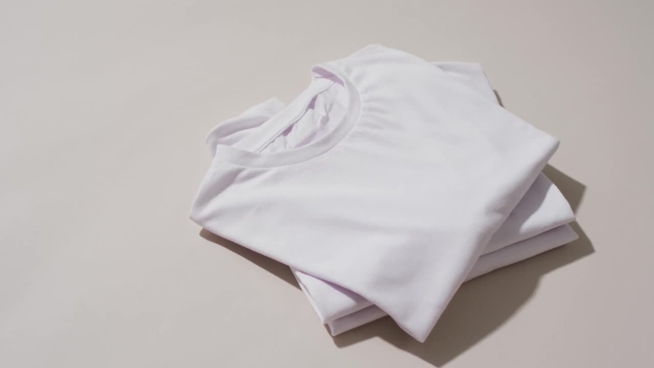 Video of stack of folded white t shirts with copy space on white background