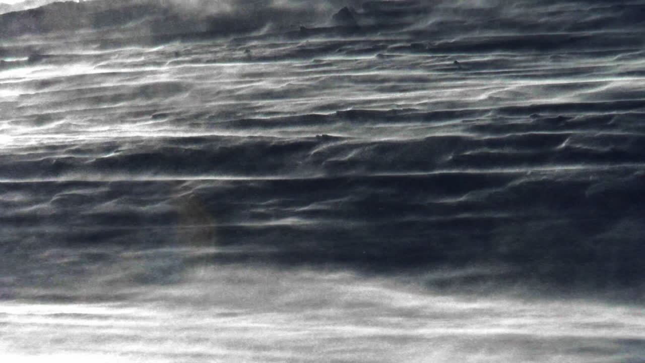 Primo piano suggestivo del terreno coperto di neve con varie texture di neve e cristalli che vengono soffiati sulla superficie durante una tempesta. Condizioni invernali estreme e dettagli alpini astratti a Saas-Fee, Svizzera.